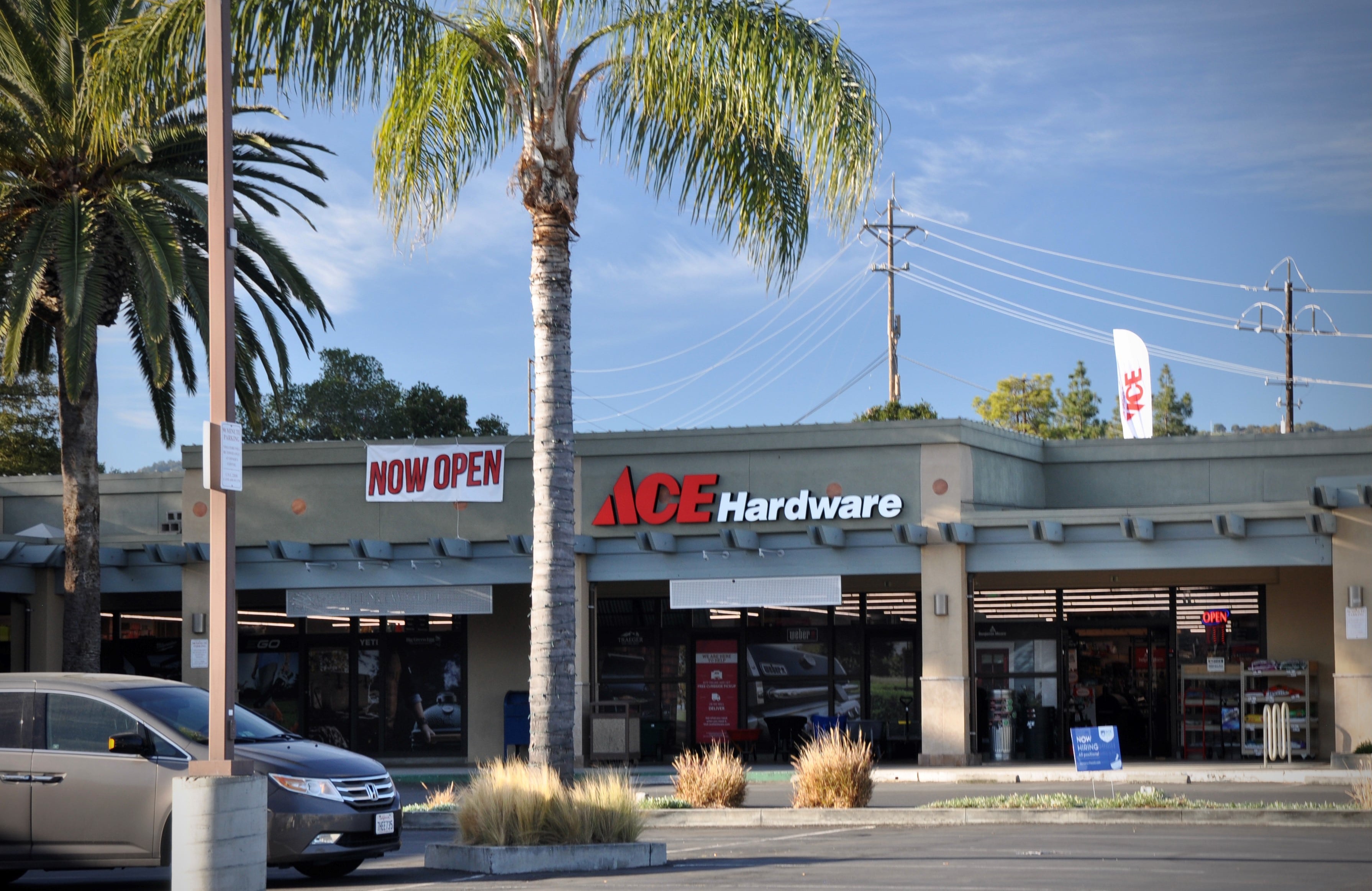 A parking lot view of the storefront signage at Ace Hardware.